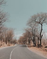 Road amidst bare trees against clear sky