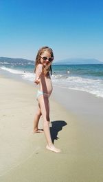Side view of shirtless girl showing thumbs up while standing on shore at beach