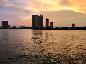 Sea by cityscape against sky during sunset