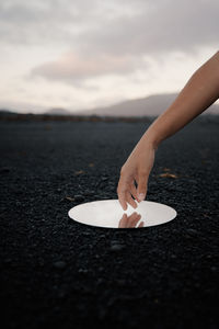 Close-up of woman hand on mirror in black sand against sky