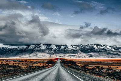 Road leading towards snowcapped mountains against sky
