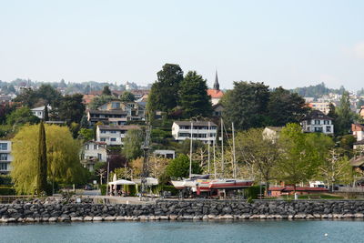 Houses by river against buildings in city against clear sky