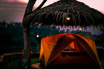 Tent by illuminated roof against sky at sunset