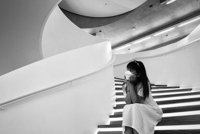 Side view of young woman sitting on the spiral stairs. 