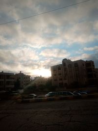 Cars on road by buildings against sky during sunset