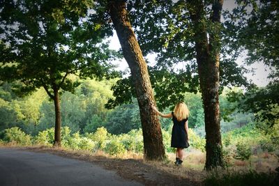 Rear view of woman standing by tree trunk