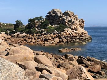 Scenic view of rocks by sea against clear sky