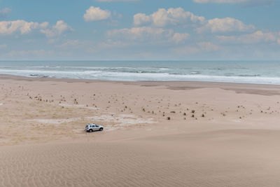 View of a vehicle in the dunes. behind more dunes, the sea and the cloudy sky.