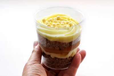 Close-up of hand holding ice cream against white background