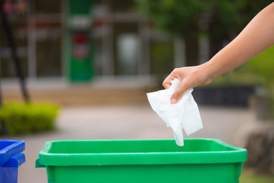 Cropped hand of person throwing paper in garbage bin