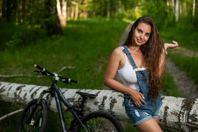 Portrait of smiling young woman with bicycle against trees