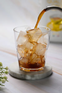 Close-up of tea being poured in glass full of ice cubes