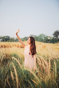 Beautiful woman with arms raised standing on field against sky