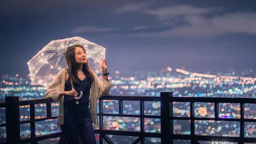 Woman standing against illuminated cityscape at night