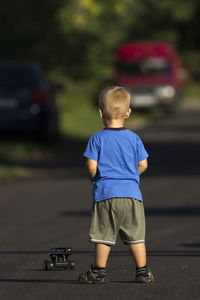 Rear view of boy standing on street and playing with toy car