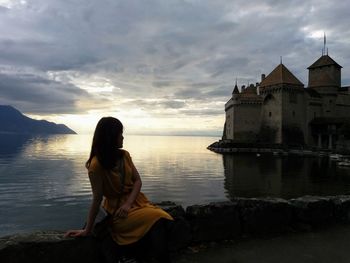 Woman sitting on retaining wall against castle in sea