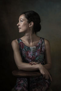 Woman looking away while sitting against black background