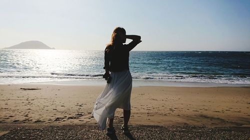 Rear view of woman standing on beach against clear sky