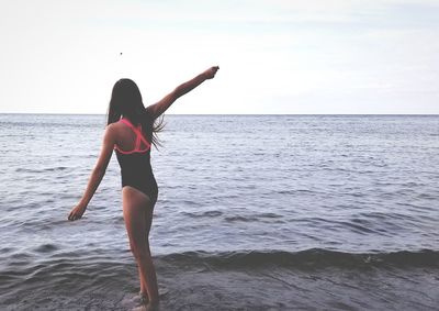 Full length of girl in swimwear standing at beach against sky