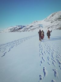 Rear view of people walking on snow covered mountain against sky