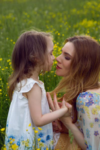 Mother and daughter in dresses and a hat stand in a field of yellow flowers in the summer day