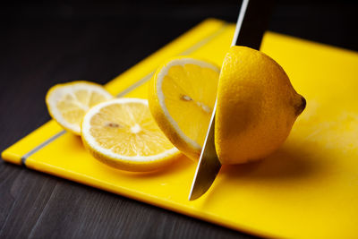 Cutting lemon in pieces, yellow cutting board on dark background