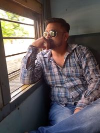 Young man looking away while sitting on window