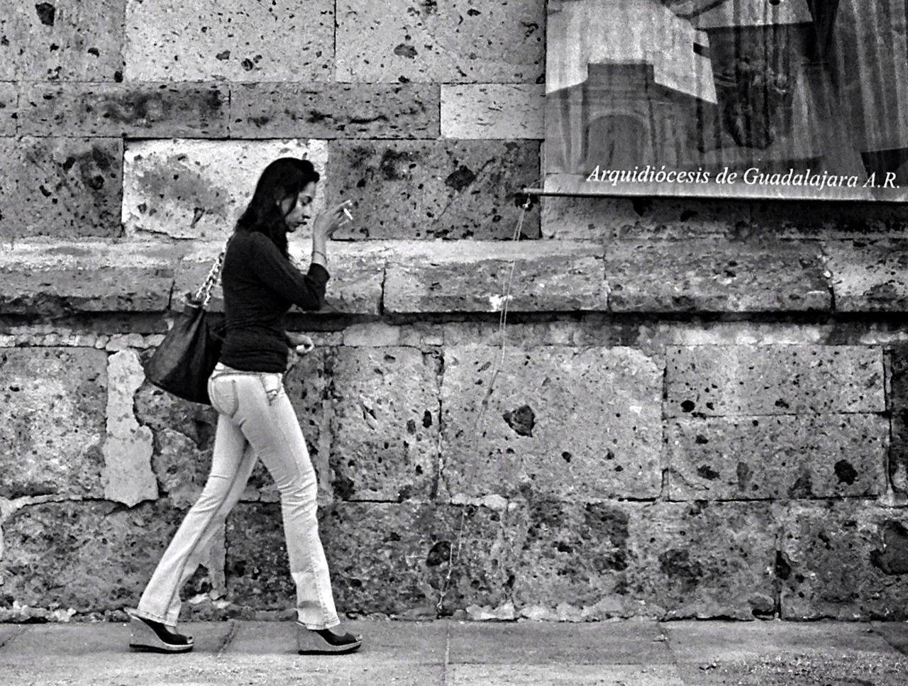 full length, casual clothing, lifestyles, young adult, person, standing, architecture, built structure, leisure activity, building exterior, wall - building feature, brick wall, side view, young women, front view, three quarter length, wall, hands in pockets