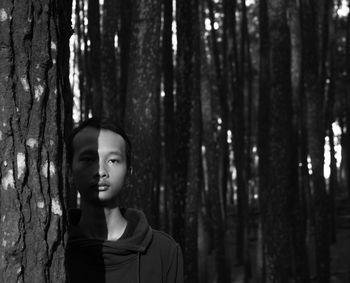 Portrait of young man standing by tree trunk in forest