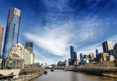 Modern buildings by river against sky in city