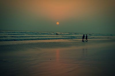 Silhouette people on beach against sky during sunset