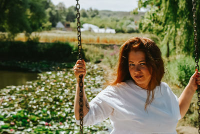 Portrait of young woman swinging against trees