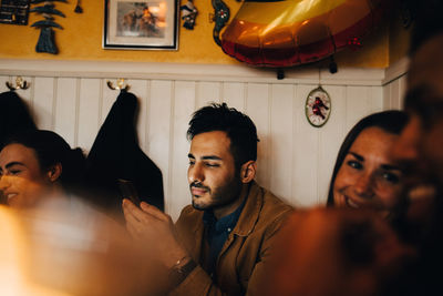 Young man using mobile phone while sitting amidst friends at restaurant