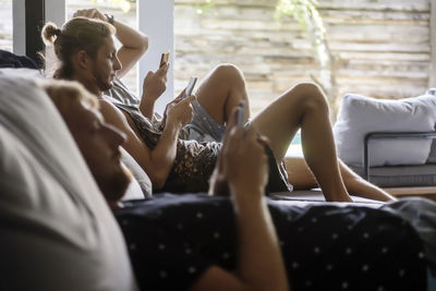 Male friends using mobile phones while relaxing on sofa at home