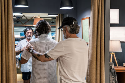 Rear view of a clothing store owner helping a customer with clothes in the clothing changing room of the store person