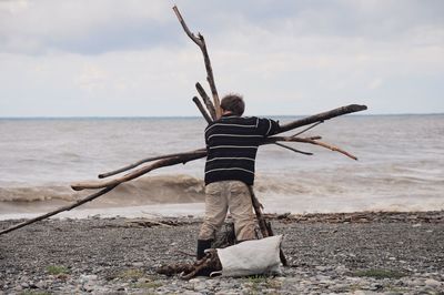 Rear view of man holding wood while standing at beach