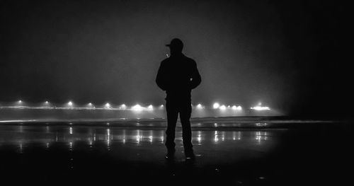 Rear view of silhouette man standing against illuminated lights at night