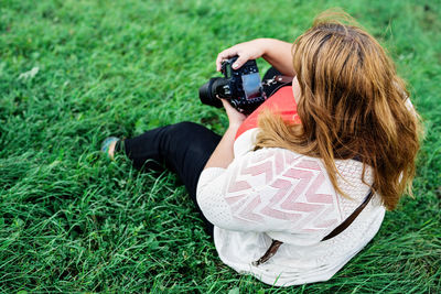 Young woman holding camera while sitting on grass outdoors