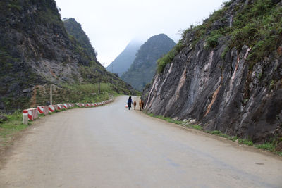 Rear view of man walking on road amidst mountains