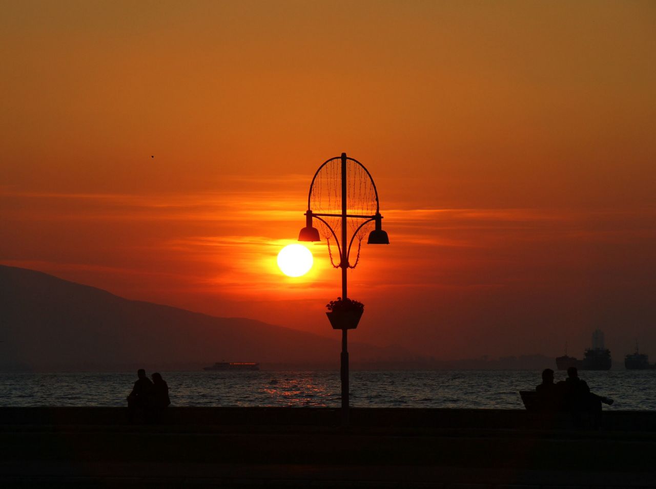 sunset, sea, silhouette, water, orange color, scenics, sky, horizon over water, beauty in nature, sun, tranquil scene, tranquility, nature, idyllic, beach, street light, unrecognizable person, outdoors, shore