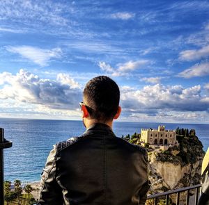 Rear view of man looking at sea against cloudy sky