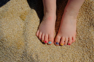 Low section of girl with colorful nail polish on sand at beach