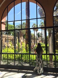 Rear view of young woman looking through window while standing in building