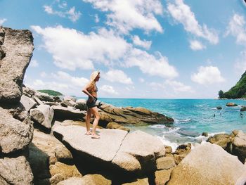 Man standing on rock by sea against sky