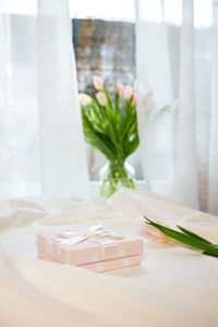 Gift box and pink tulip on a white blanket and a bouquet in a vase on the window. nice morning