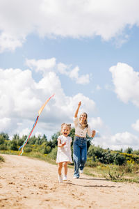 A laughing little girl and her mother run along the road to the field and fly a kite. 