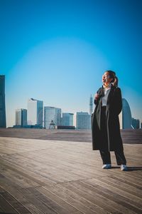 Full length of man standing on mobile phone against blue sky