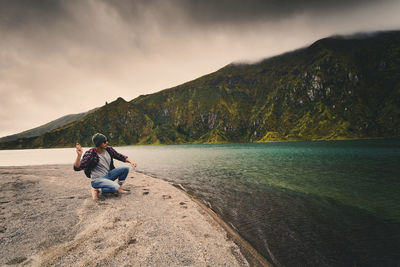 Man throwing stone in lake by mountains