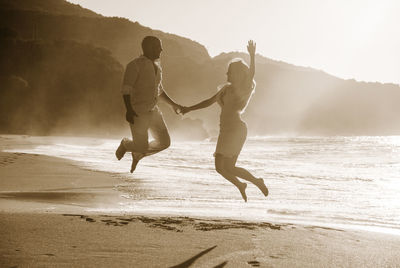 A couple jumps on a beach during sunset