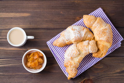 Fresh croissants, a cup of coffee and jam in a bowl on a wooden table. brunch and coffee break